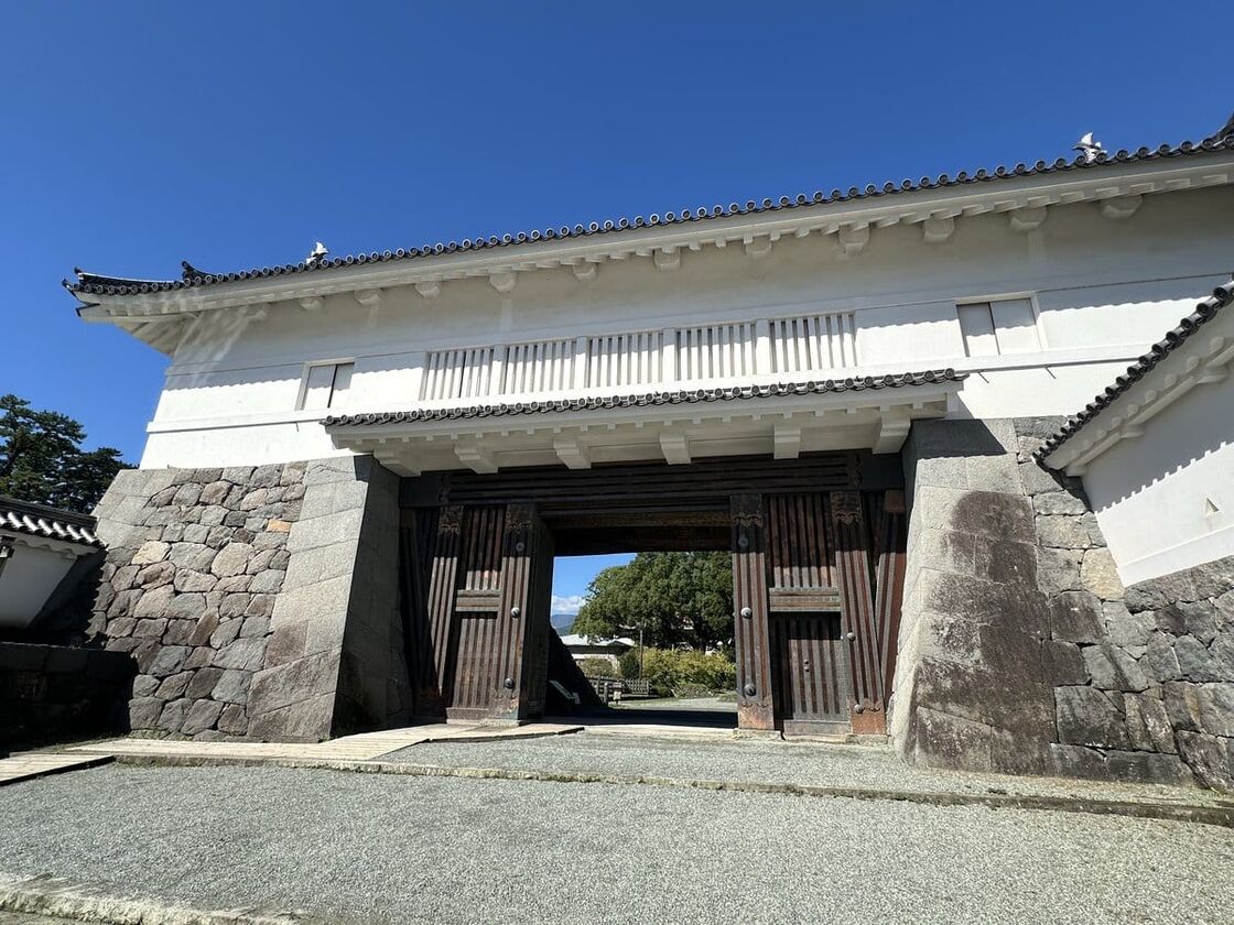白壁の櫓門を正面から見上げた様子。奥に松の木と青空